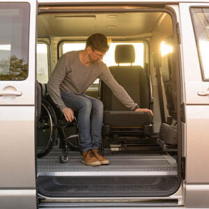 Personne se transférant depuis son fauteuil roulant vers le siège conducteur de son véhicule grâce à une embase pivotante Six Way, le tout à l'intérieur de son véhicule PMR.