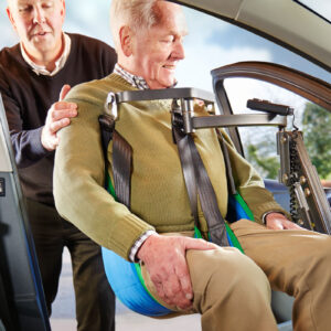 Un homme se faisant transférer de son fauteuil roulant à la place de passager avant d'une voiture grâce à un soulève personne installé dans la voiture.