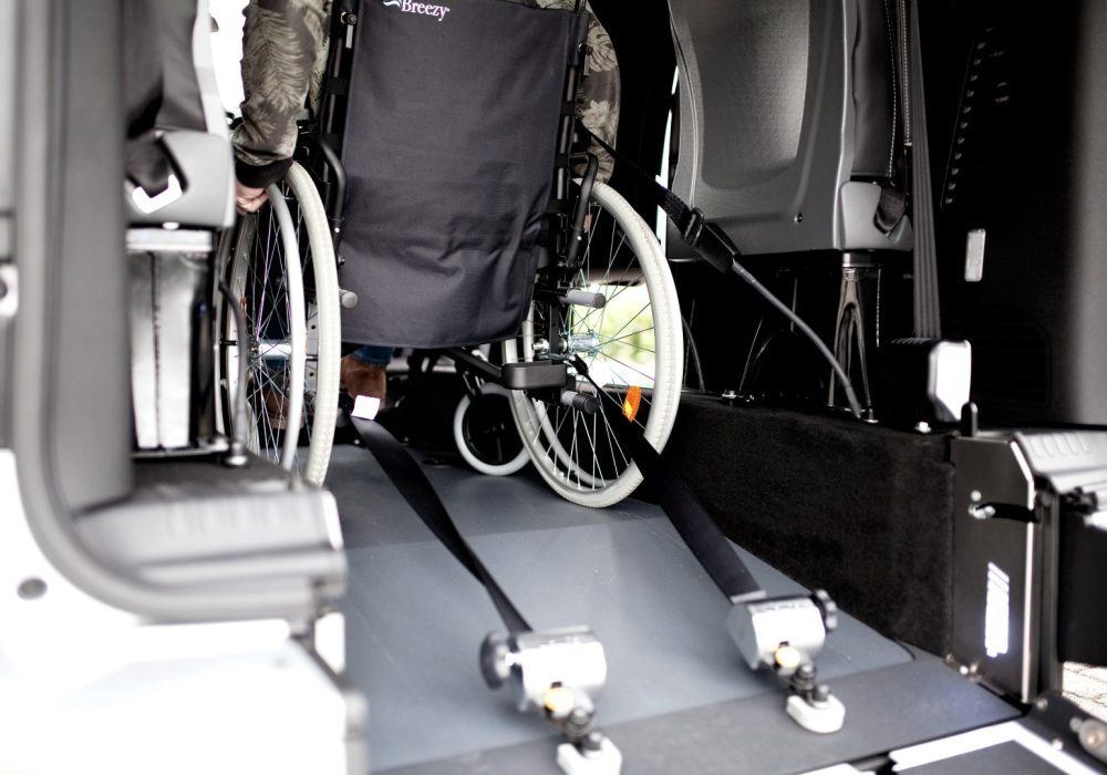 Personne en fauteuil roulant installée à bord d'un Peugeot Traveller M TPMR au niveau de son décaissement avec sa rampe déployée - véhicule TPMR - voiture handicap