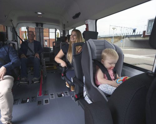 Différentes personnes installé dans un minibus TPMR aménagé avec le plancher Triflex Air dont un enfant dans un siège enfant et une personne en fauteuil roulant